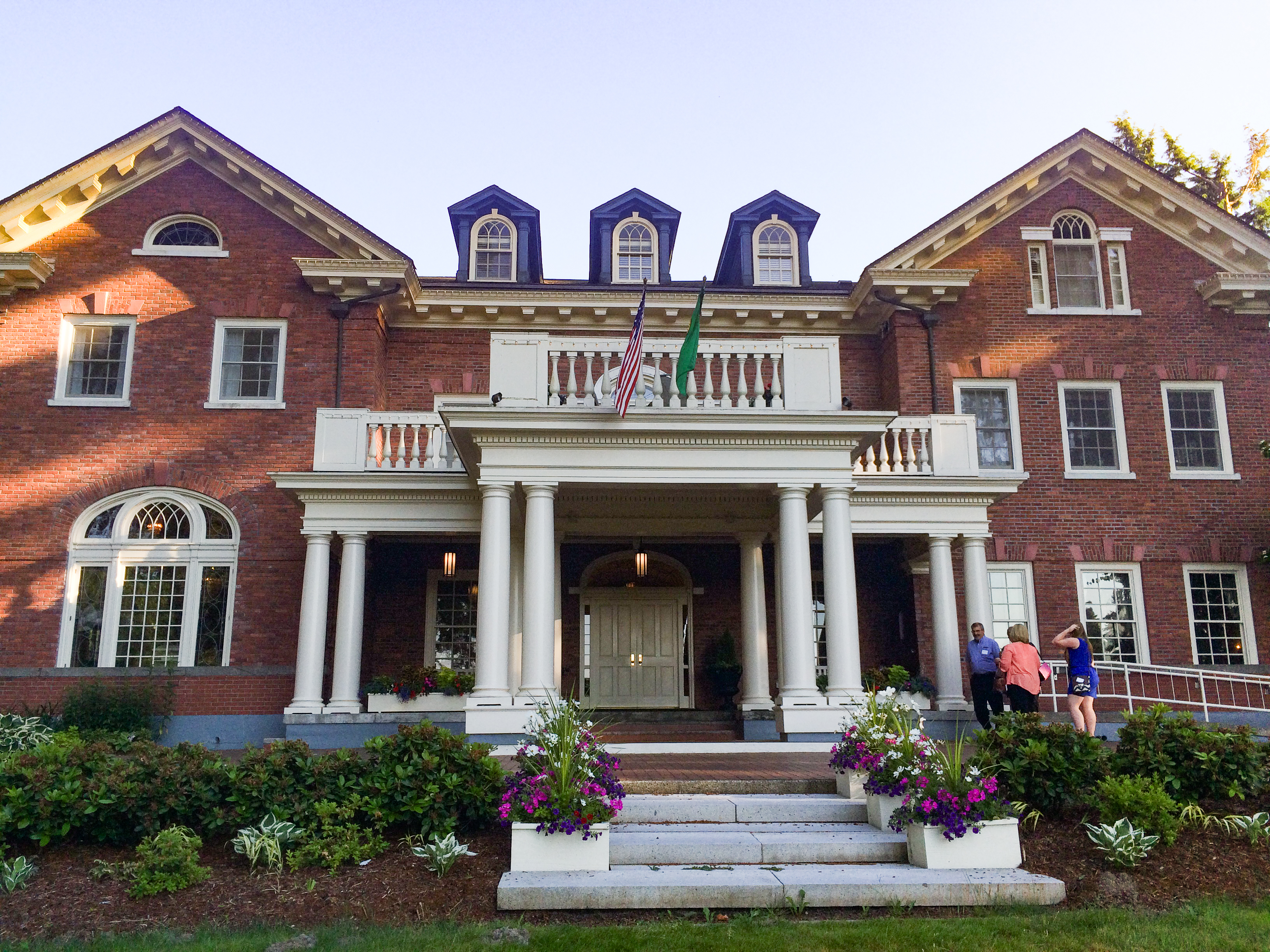 The front side of the Governor's Mansion, which is made of red bricks and white accents. An American flag and Washington State flag hang above the front porch.