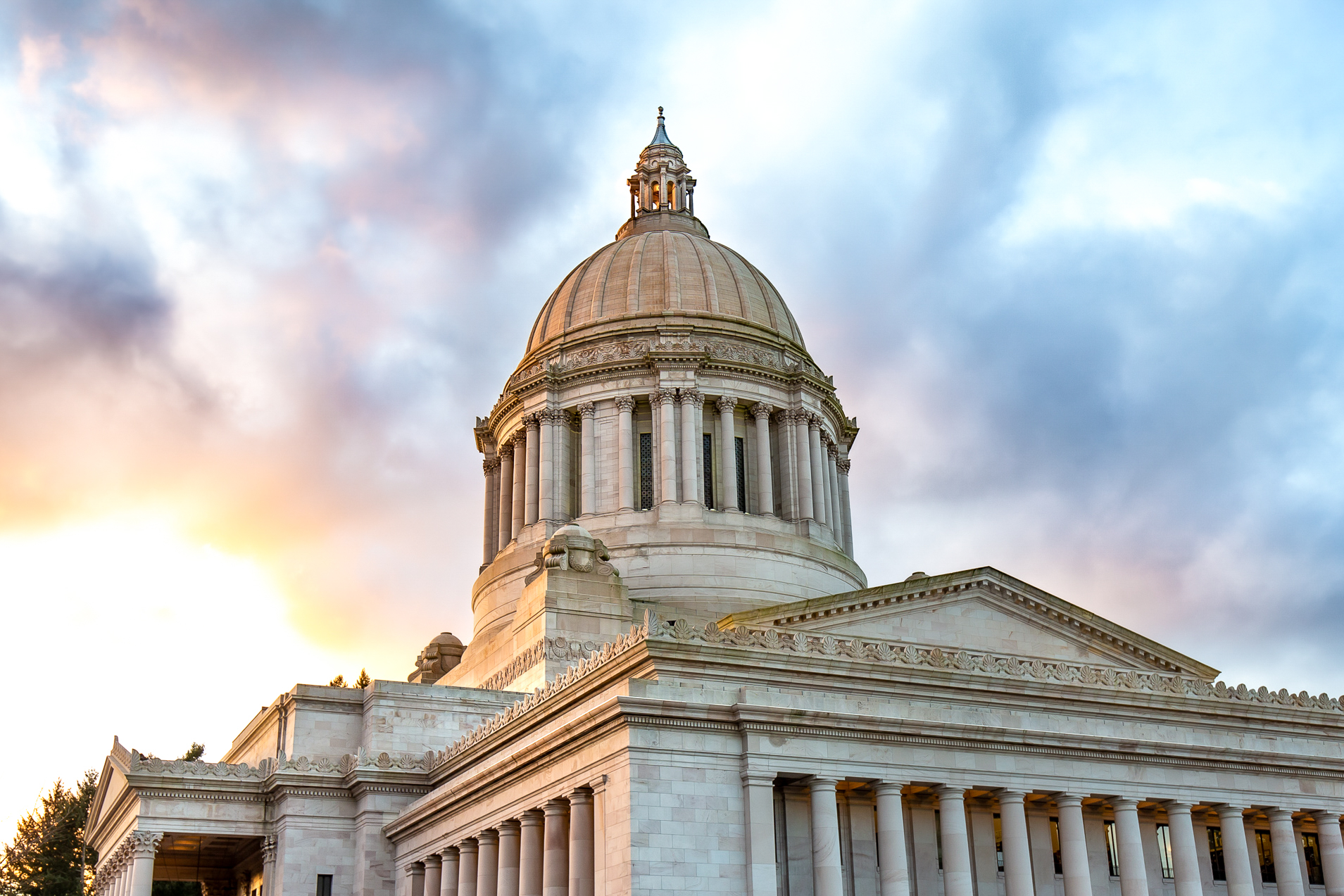 The Legislative Building dome being lit up by a sunset with a blue and yellow cloudy sky in the background.