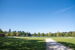 A nature scene with gravel pathways leading through open, green lawns with trees, the Legislative Building, and a clear, blue sky in the distance.