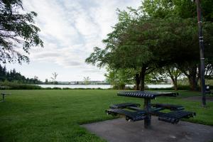 A nature scene with a metal picnic table in the foreground set off a green lawn lined with trees and a small glimpse of Capitol Lake and downtown Olympia in the distance.