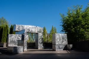 The Untitled Stainless Steel Statue reflects the sunlight while its sharp, geometric shapes contrast against the natural shapes of the trees behind it.