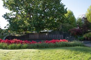 A nature scene with red flowers in the foreground surrounding the Vietnam Veterans Memorial with a large green tree and floral bushes in the background.