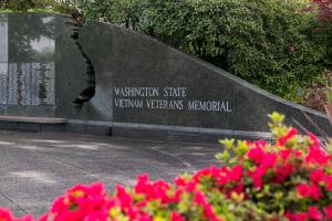 A close-up with red flowers in the foreground and a dark granite wall inscribed with the text "Washington State Vietnam Veterans Memorial" in the background.