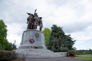 An outdoor scene with flowers placed on the steps of the Winged Victory Monument with trees and an American flag in the background.