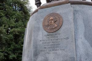 A close-up of the bronze Washington State Seal set into the granite base of the Winged Victory Monument with trees in the background.