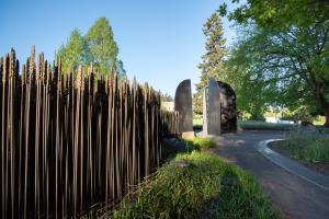 A nature scene with a bronze wheat patch in the foreground next to a stone pathway that leads to the World War II Memorial's bronze blades, surrounded by large green trees.