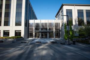 The 1500 Jefferson building entrance, made with large, glass walls and metal framing. A wide, concrete walkway lined with large square rocks, trees, and a street lamp.