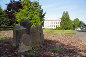 A close up of the Eastern Washington Cultural Landscape Garden's basalt rock columns, with various trees, the Insurance building, and part of the South Diagonal visible in the background.