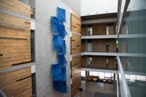 A view of the Hydro Logic, a blue aluminum sculpture, from the third floor of the Helen Sommers building. The sculpture is on a concrete wall between wooden panels and across glass office walls.