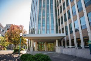 The south entrance to the Highways-Licenses Building, with the numbers "1125" above the doors. A small concrete plaza with green shrubs and a reddish-orange trees sits between this entrance and the Natural Resources Building entrance.