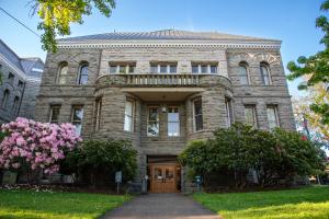 A view of the Old Capitol Building's ADA-accessible entrance, which is located on the north side of the building. Trees with pink flowers are on both sides this entrance, which is framed by two short, cylindrical towers and a stone balcony.