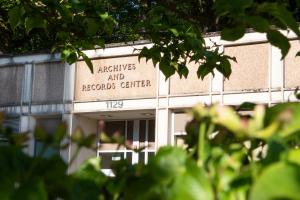 Green leaves frame the metal lettering set into brown stone that spells "Archives and Records Center" above the State Archives Building entrance.