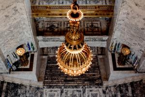 An overhead view of the large chandelier that hangs over the Legislative Building Rotunda. The Roman firepots, stairs, and third- and fourth-floor balconies are in the background.