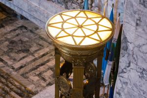 An overhead view of the top of a Roman firepot, which features bronze framing in the shape of a sun and yellow light shining through pale glass.