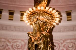A close-up of the upper portion of large chandelier in the Legislative Building Rotunda. This section features two angels under a single row of small lightbulbs.