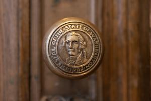 A Washington State Seal embossed into a bronze doorknob on a wooden door.