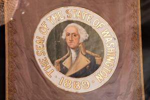 A painted Washington State Seal on an old Washington State flag. The seal features a full-color portrait of George Washington and gold lettering.