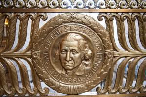 A Washington State Seal embossed into a bronze railing, which also features an embossed wreath and plant patterns.