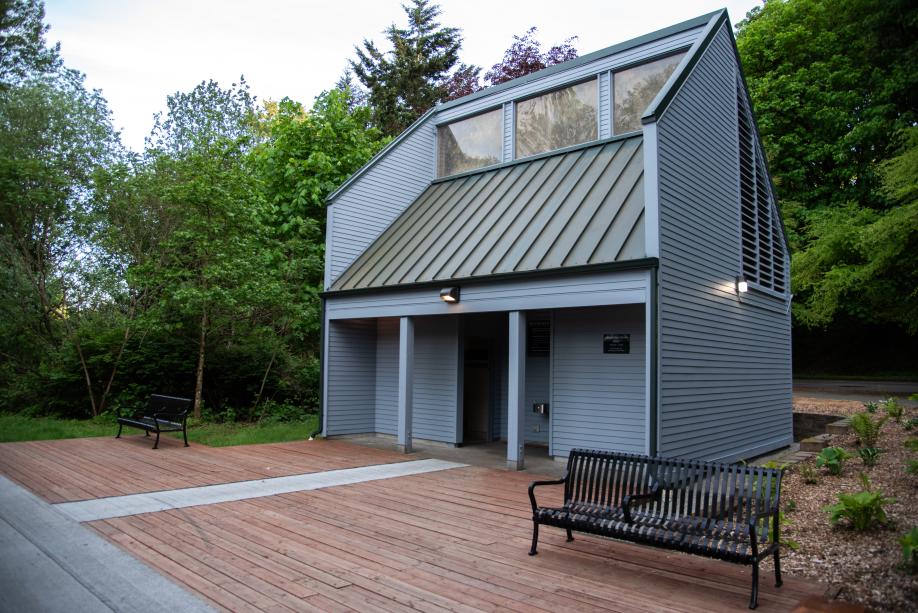 An outdoor scene with two metal park benches set on a wooden deck that leads to a new-looking wooden building (the Interpretive Center restrooms).