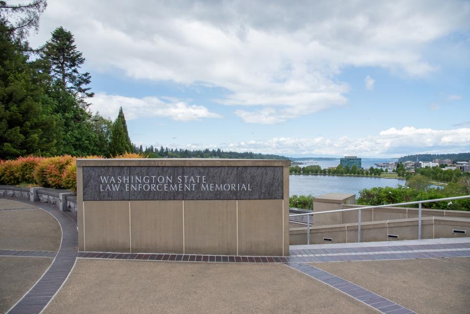 A cement and granite wall inscribed with the words "Washington State Law Enforcement Memorial" with trees, Capitol Lake, and downtown Olympia in the background.