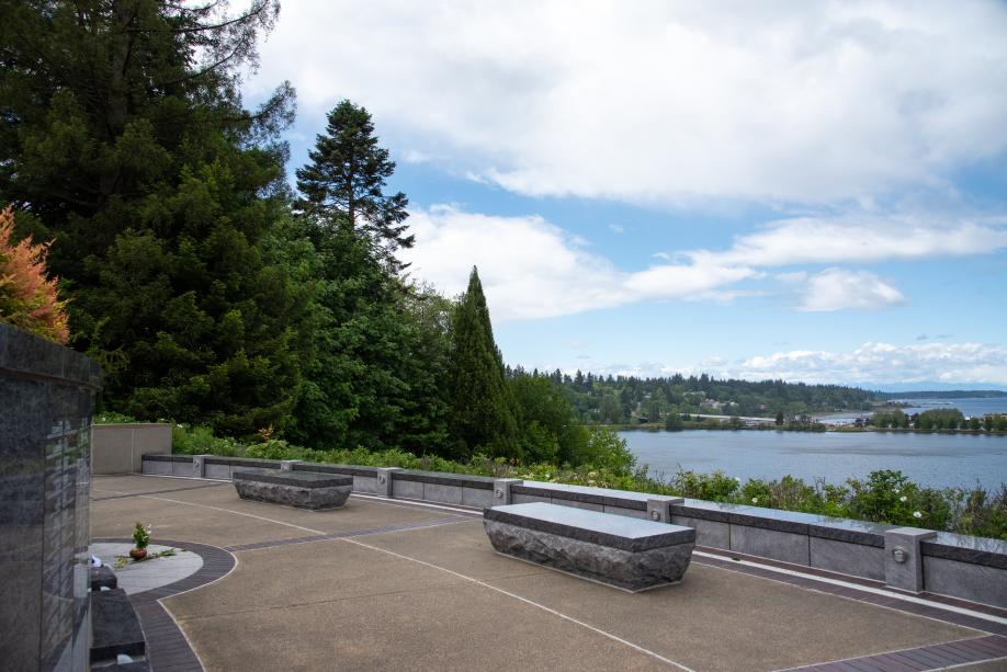 An outdoor scene with two granite benches overlooking Capitol Lake and downtown Olympia, with large trees in the background.