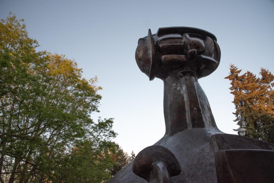 The piece at the top of the Shaman Statue has a strong, dark silhouette against the light blue sky and the vibrant trees around it.