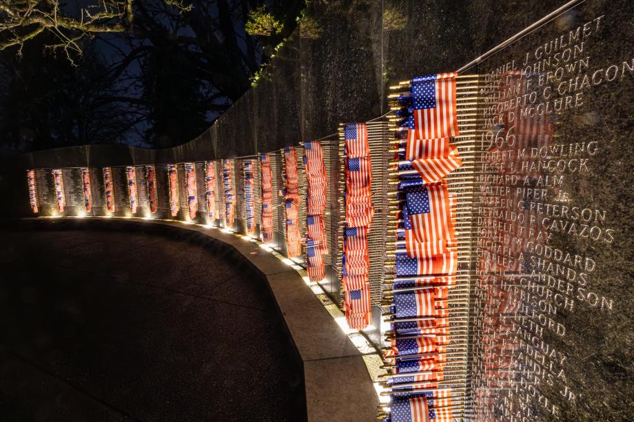 A close-up of the names inscribed the Vietnam Veterans Memorial with small American flags set into the wall and lights shining on them.