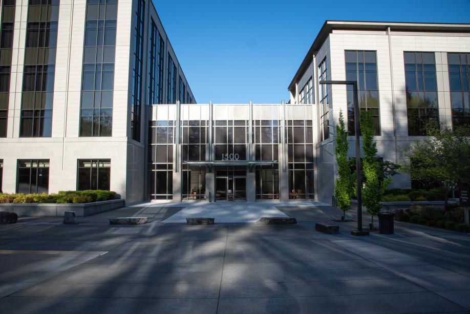 The 1500 Jefferson building entrance, made with large, glass walls and metal framing. A wide, concrete walkway lined with large square rocks, trees, and a street lamp.