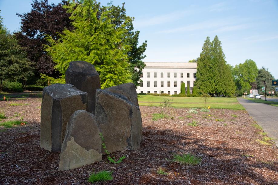 A close up of the Eastern Washington Cultural Landscape Garden's basalt rock columns, with various trees, the Insurance building, and part of the South Diagonal visible in the background.