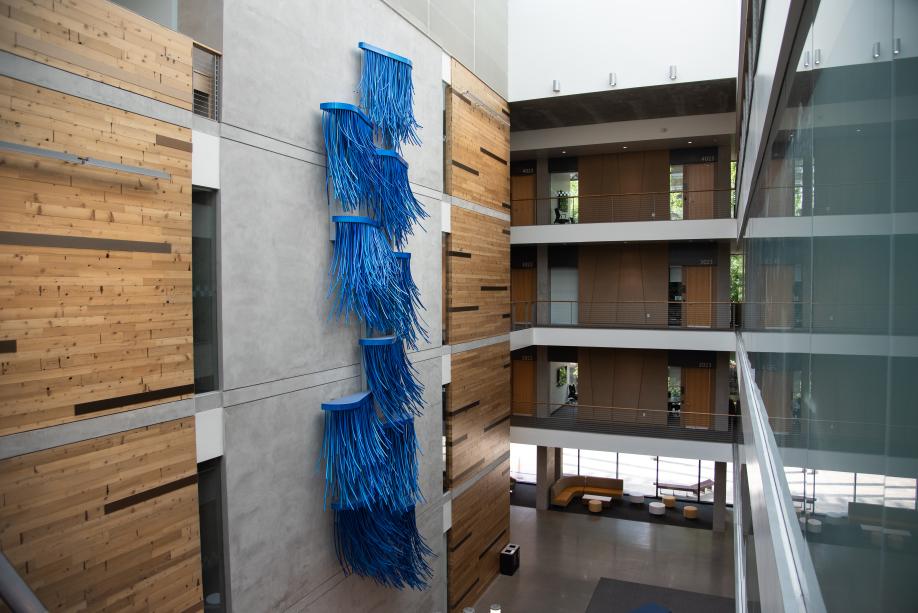 A view of the Hydro Logic, a blue aluminum sculpture, from the third floor of the Helen Sommers building. The sculpture is on a concrete wall between wooden panels and across glass office walls.