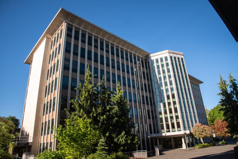 A view of the Highways-Licenses Building from the southwest. This side of the building stands tall next to various green trees, as well as reddish-orange trees.