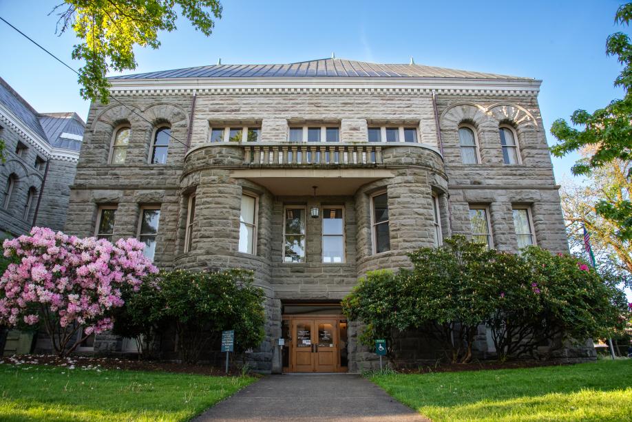 A view of the Old Capitol Building's ADA-accessible entrance, which is located on the north side of the building. Trees with pink flowers are on both sides this entrance, which is framed by two short, cylindrical towers and a stone balcony.