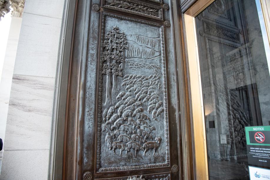 A bronze door with a carved image of a sheep herd grazing in a valley.