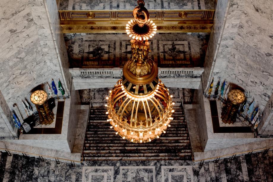 An overhead view of the large chandelier that hangs over the Legislative Building Rotunda. The Roman firepots, stairs, and third- and fourth-floor balconies are in the background.