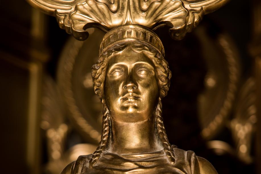 A close up of a small sculpture on a Roman firepot, which depicts an expressionless woman with a floral headress.