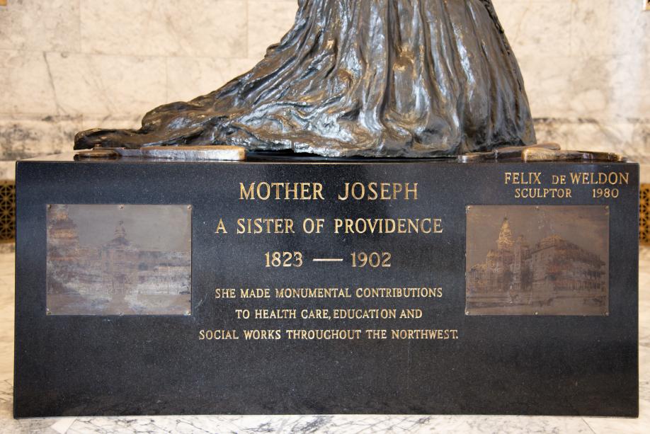 A rectangular, black granite platform inscribed with information about Mother Joseph. Two etched pictures of old buildings are on metal plaques on the sides of the inscribed text.