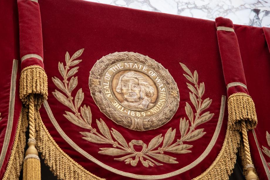 A gold Washington State Seal and wreath embroidered into red curtains.