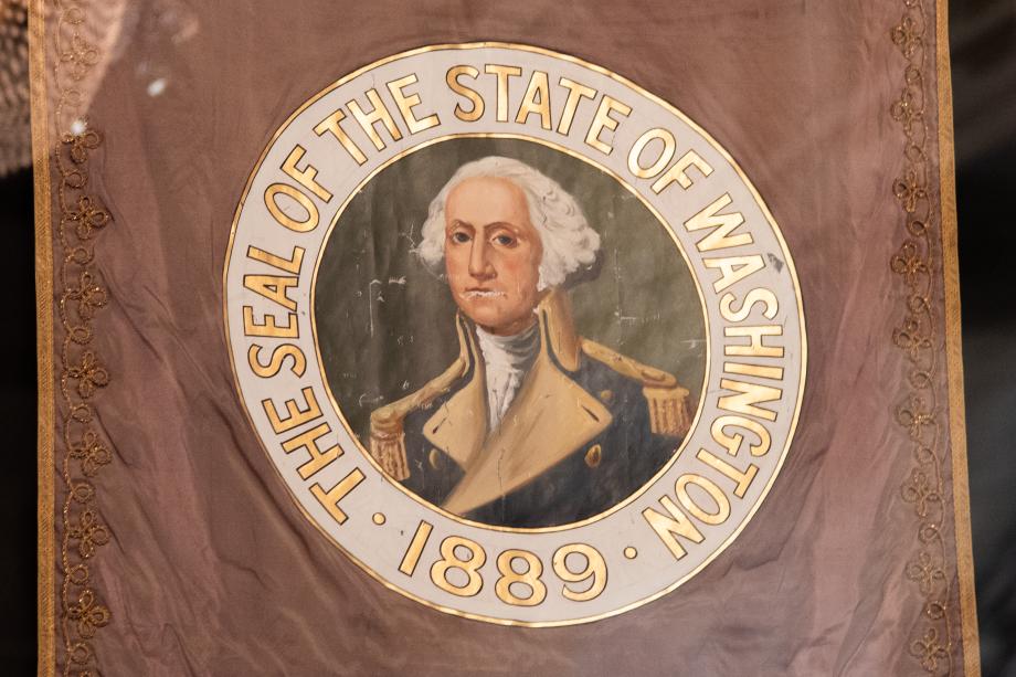 A painted Washington State Seal on an old Washington State flag. The seal features a full-color portrait of George Washington and gold lettering.