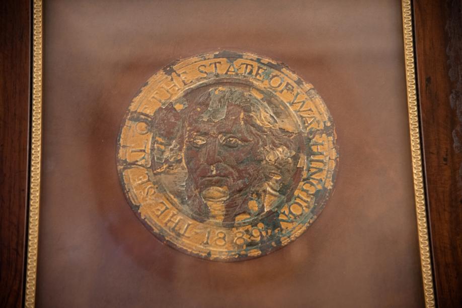 A framed piece of leather with faded and torn Washington State Seal embossed into it.
