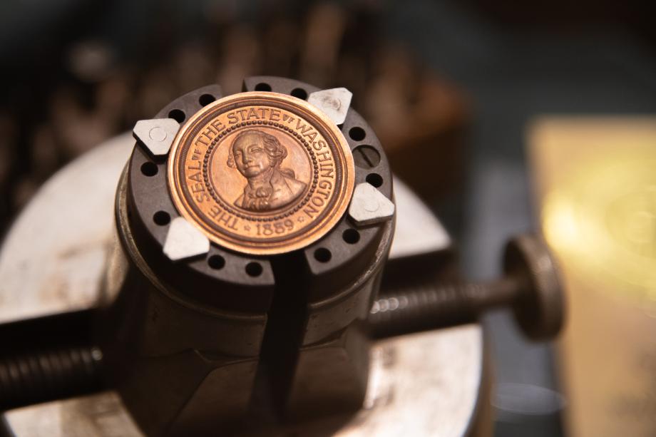 A close up of a tiny bronze Washington State Seal on the end of a stamping die.