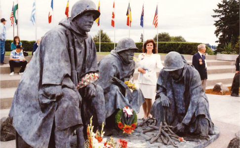 A photo of Ms. Fellows, dressed in a white suit, standing with her sculpture commemorating the Korean War.