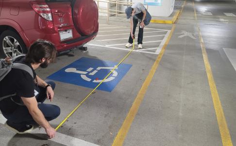 2 DES staff employees measuring the width of an ADA parking spot with a measuring tape.