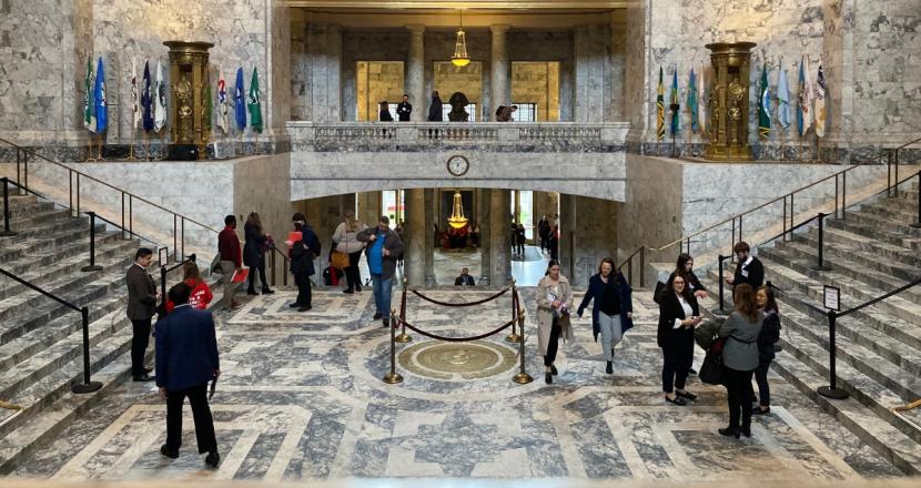 People walking around and taking photos of the Legislative Building's interior, which is primarily marble with gold accents.