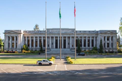 A wide shot of the Temple of Justice with three flagpoles and small trees in front of it.