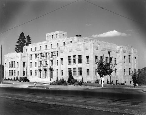 A black and white image of the Capitol Court Building from across the street. A single black car is parked in front of the square, white stone building.