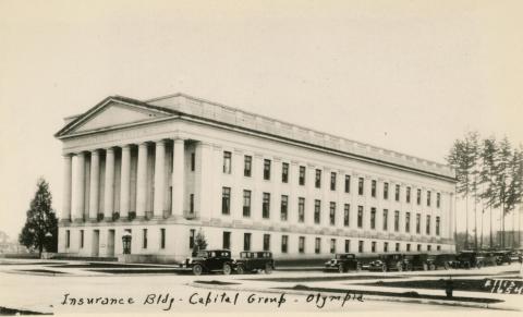 A black and white image of the Insurance Building with black cars parked along the street. Writing at the bottom of the photo says "Insurance Bldg - Capitol Group - Olympia."