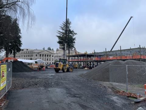 A wide shot of the Irving R. Newhouse Building construction site, showing the building's steel framework surrounded by piles of gravel, heavy construction equipment, and metal fences.