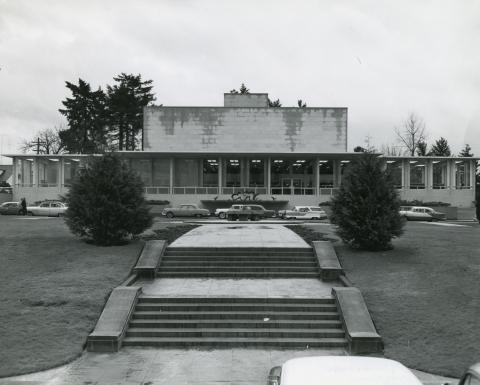 A black and white image of the front side of the Pritchard Building from the plaza across the street. A stone pathway and stairs lined with small shrubs lead up to the building's entrance.