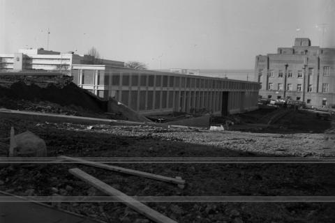 A black and white image of the State Archives Building during construction. The building's fresh facade is surrounded by piles of dirt, and the Capitol Court Building is visible in the background.