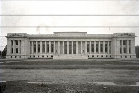 A black and white image of the front side of the Temple of Justice. The building stands alone on a plot of dirt and gravel.